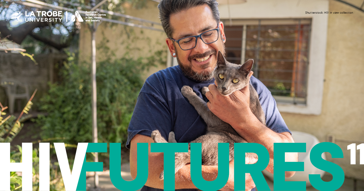 A middle-aged man with blue framed spectacles and silver plug earrings, standing in a back garden, holding and smiling at a Russian Blue cat, with text 'HIV FUTURES 11'