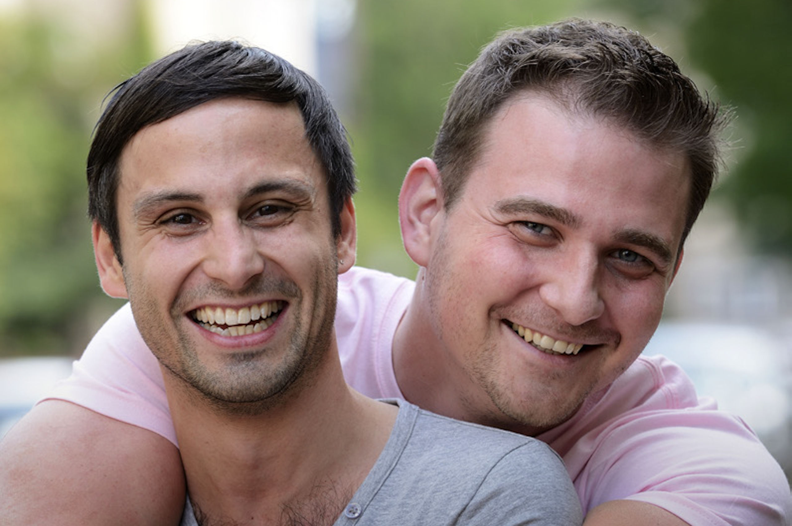 The Influence of AFAO, AIDS Councils & Communities Two masculine people hugging, smiling and looking at the camera