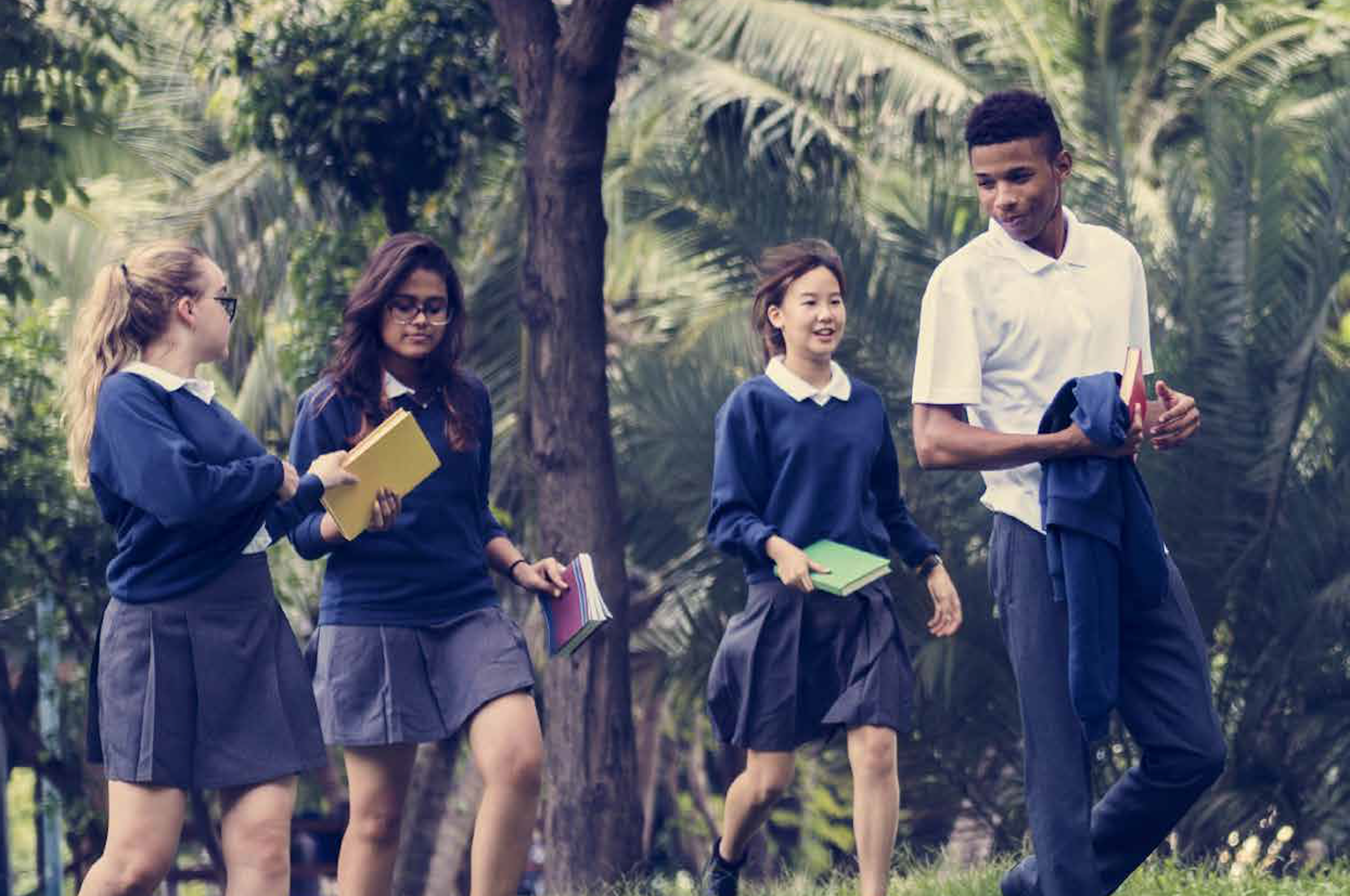 Four teens in school uniform talking, walking through a park with palm trees 