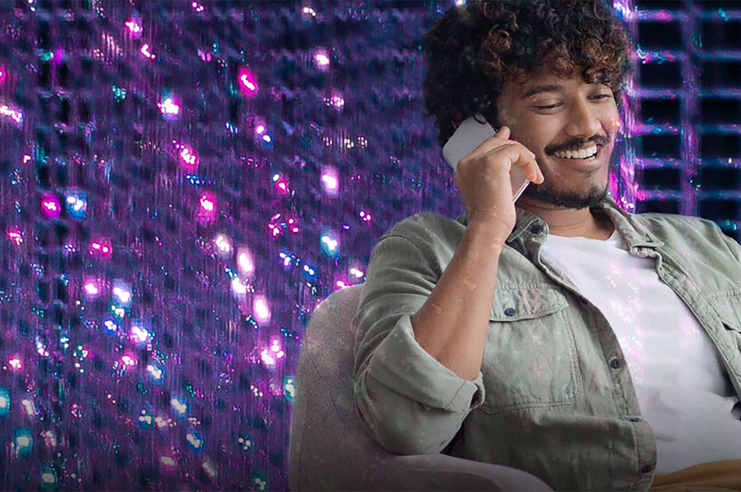 A young man sitting down, talking on a phone and smiling