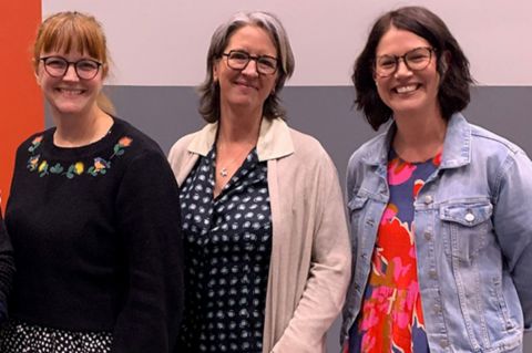 Three women smiling at the camera in front of a graphic wall
