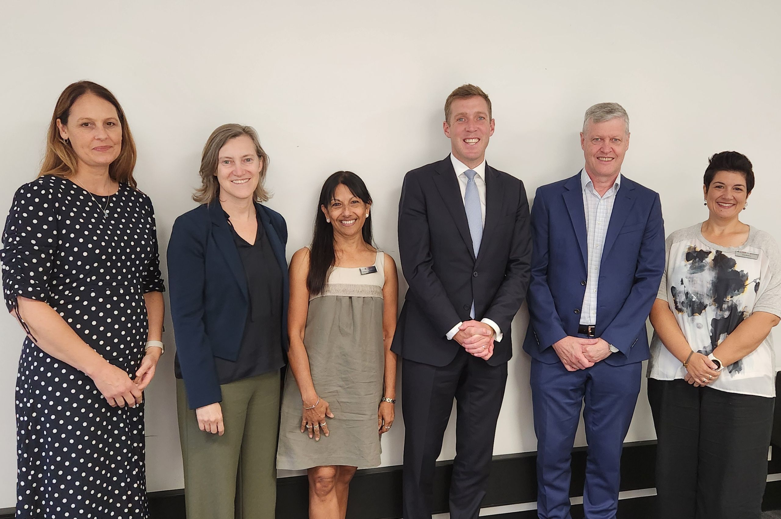 A group of people stands united in front of a white wall, displaying a sense of community and togetherness