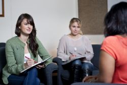 three females sitting in chairs, two taking notes as talking